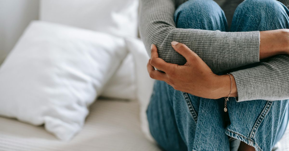 pessoa sentada de calça jeans com blusa cinza abraçando os joelhos e administrando sua ansiedade