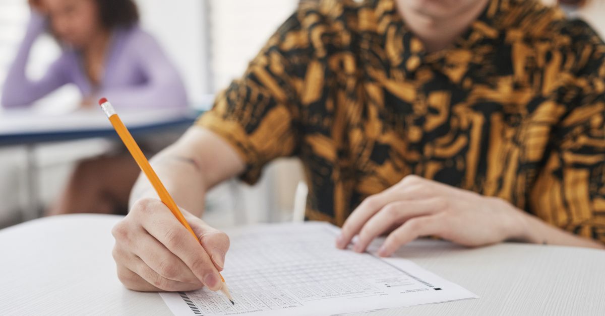 jovem de camisa amarela e preta, com lápis na mão realizando uma prova e utilizando as dicas úteis sobre concursos