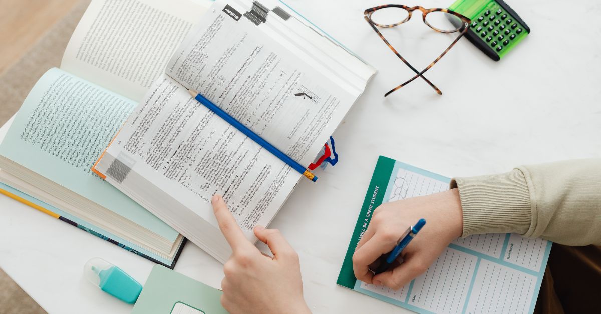 braços em cima de uma mesa com livros lápis e calculadora focando em estudos e produtividade