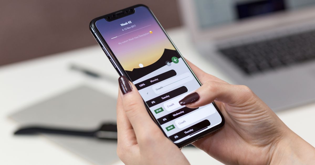 mulher com esmalte escuro nas unhas mexendo no celular buscando os melhores aplicativos para sua rotina
