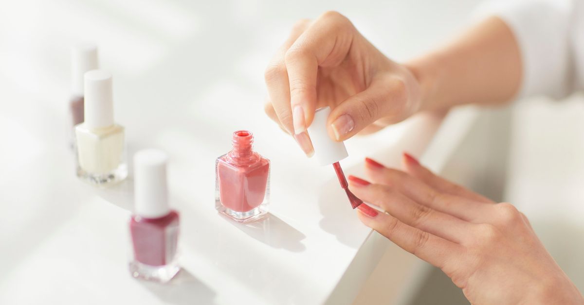 uma mulher passando um esmalte de tom rosado nas unhas, mostrando cuidado que devemos ter para conquistar unhas fortes