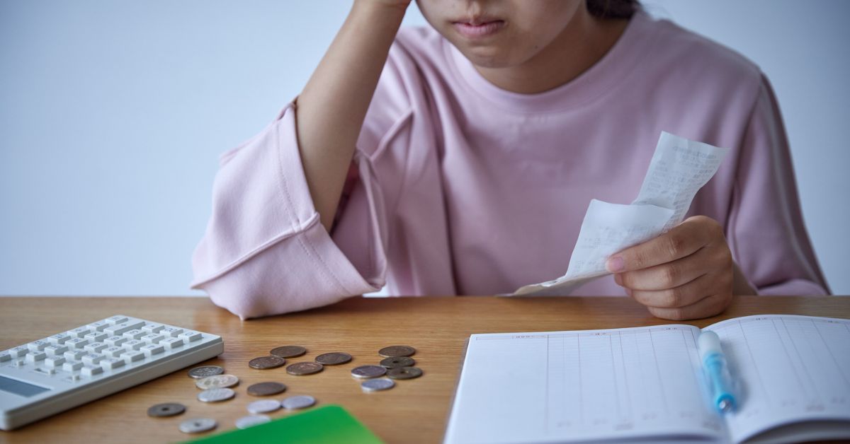 mulher com camiseta rosa, segurando um papel, com o braço apoiado em uma mesa com mordas, calculadora, com a sensação de que gastou mais do que deveria