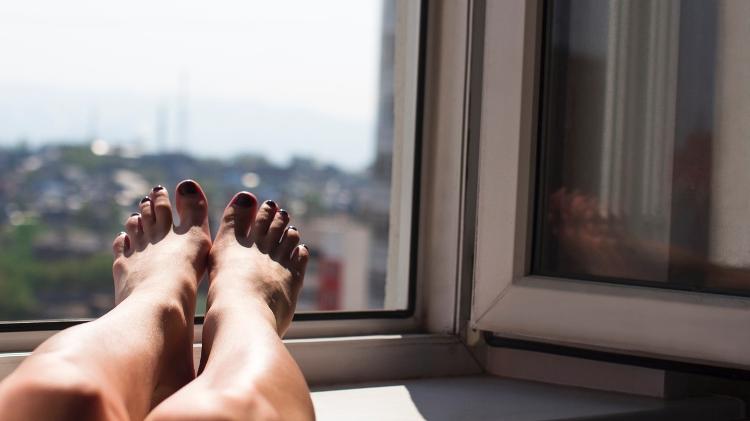 pés com esmalte preto nas unhas, apoiados em uma janela tomando sol