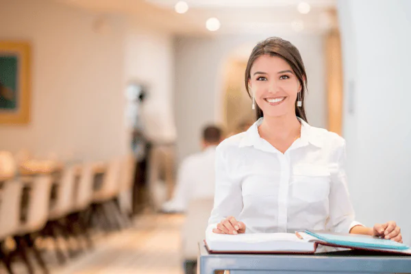 Mulher com uma camisa branca sentada em uma mesa com um livro aberto procurando trabalho de freelancer