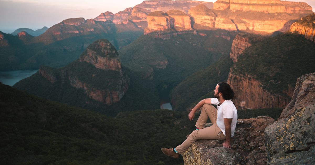 homem com camiseta branca, sentado em uma montanha, praticando turismo de bem-estar